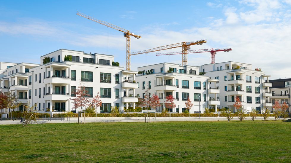 Brandneue Luxus-Reihenhäuser und klarer Himmel in Düsseldorf, Deutschland, drei Kräne eines Baugebiets hinter den Gebäuden