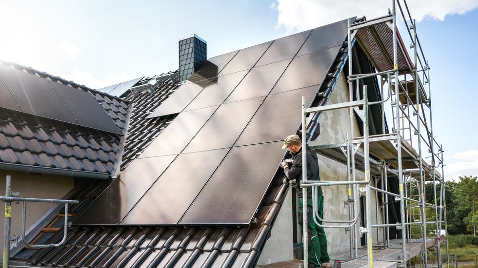 Techniker steht auf einem Gerüst, während er an einem Solarpanel eines Einfamilienhauses in Deutschland arbeitet.
